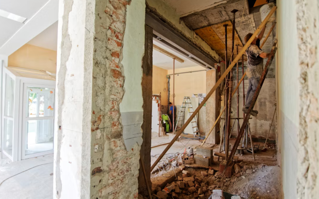Home renovation in progress with exposed brick walls and construction workers installing structural supports.